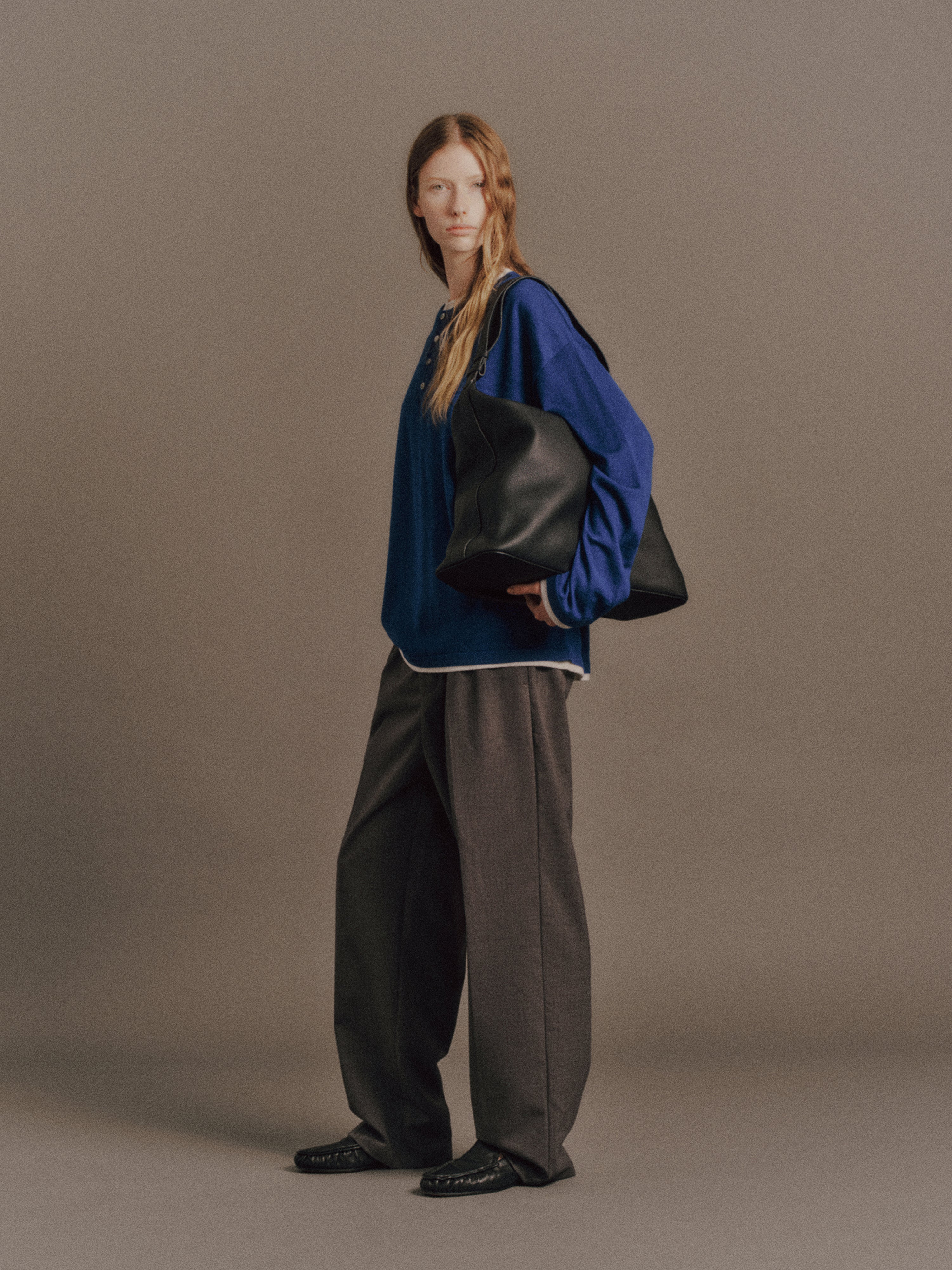 Tyla wears Austin Sweater in Blue, Carlos Pant in Grey, Cow Leather Aura Bag In Black