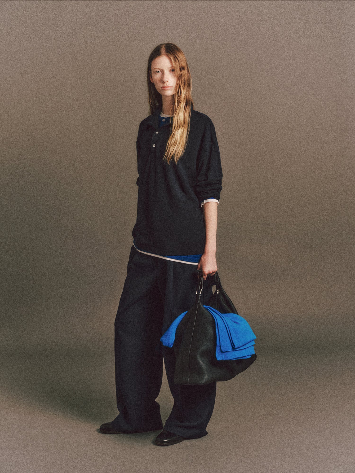 Tyla wears Austin Sweater in Blue, Aurora Top In Dark Navy, Luka Pant in Dark Navy, Molly Scarf In Blue, Cow Leather Aura Bag In Black