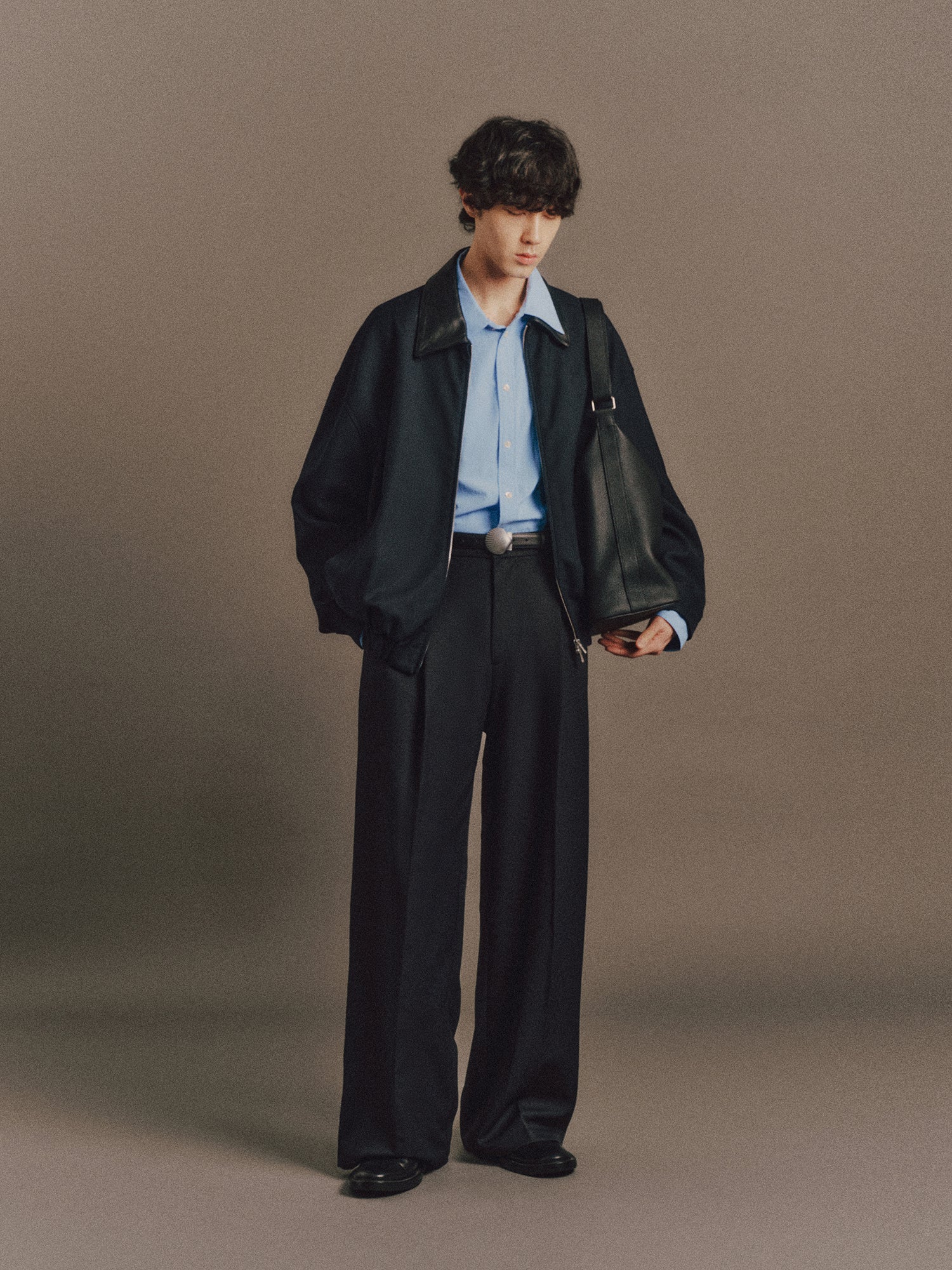 Émile wears Haley Shirt In Light Blue, Krauter Jacket In Dark Navy, Luka Pant In Dark Navy, Shell Belt In Matt Silver, Cow Leather Aura Bag In Black