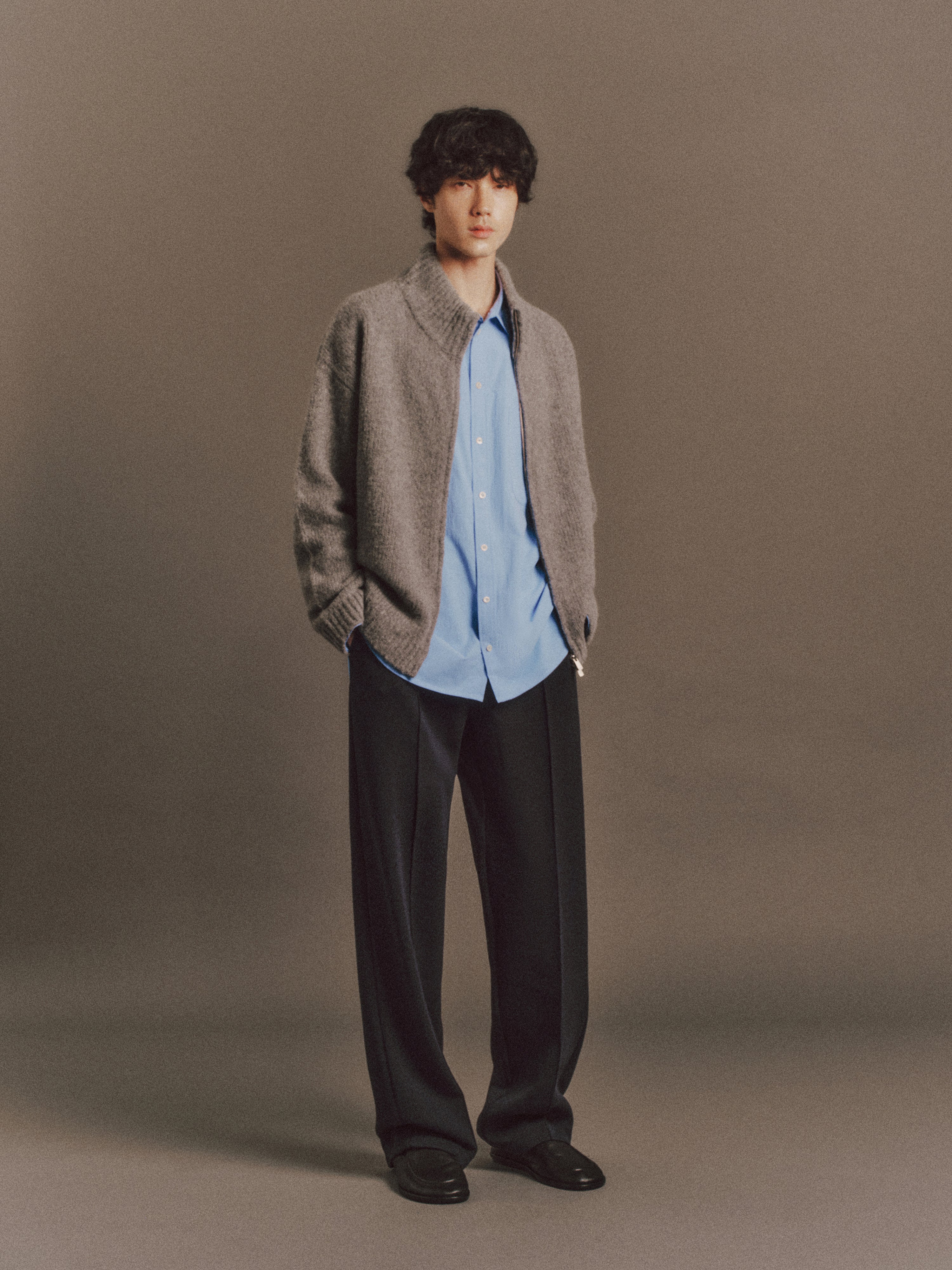 Émile wears Haley Shirt In Light Blue, Yannick Sweater In Grey, Nova Pant In Dark Navy.