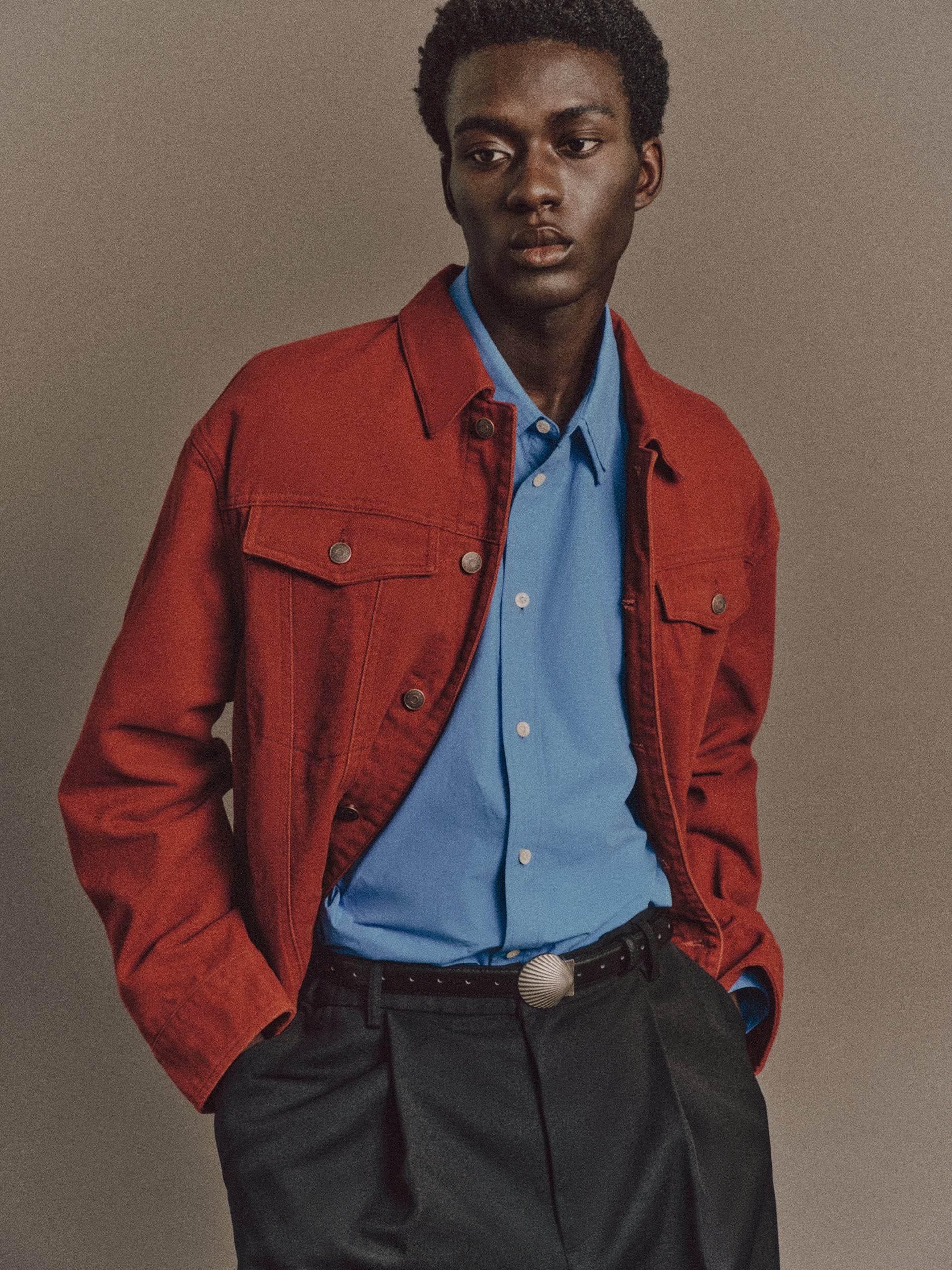 Muhamed wears Burt Shirt In Blue, Noel Jacket In Red, Luka Pant In Black, Shell Belt In Vintage Silver