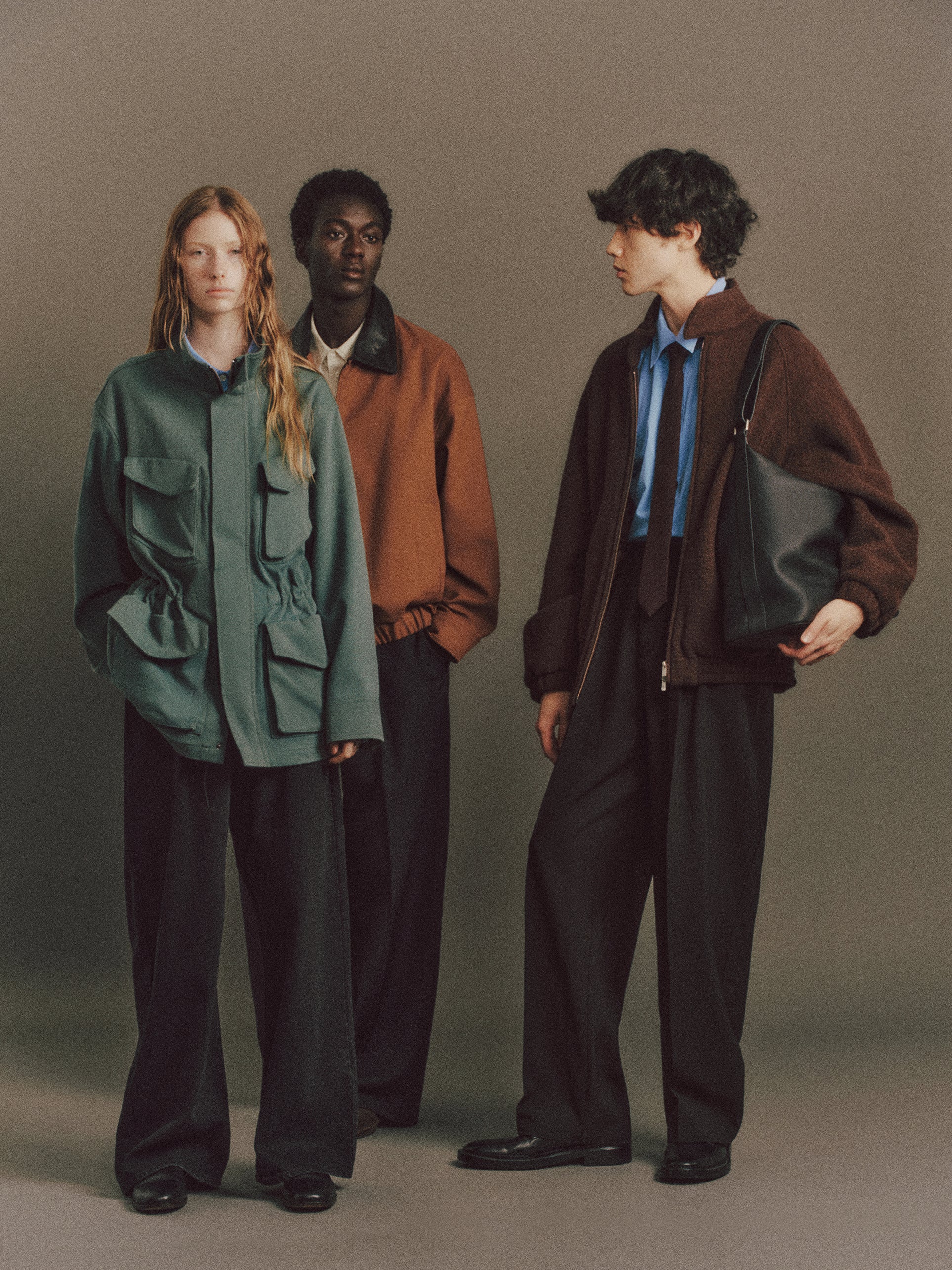 Three people standing against a plain background, wearing stylish outfits.